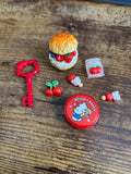 Collection of small toys including a red container with a bear design, a key, and other items on a wooden surface.