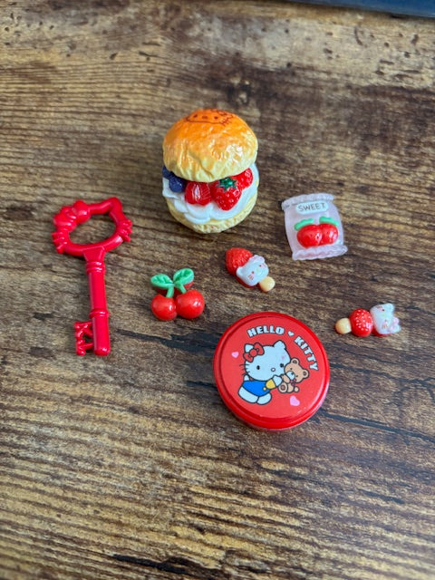 Collection of small toys including a red container with a bear design, a key, and other items on a wooden surface.