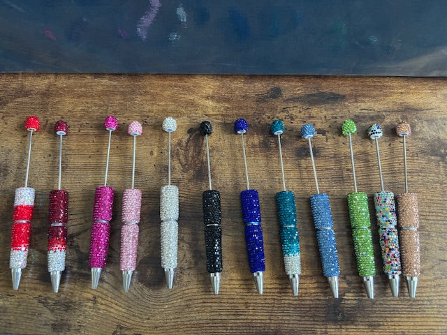 Assorted colorful pens with bead accents on a wooden surface