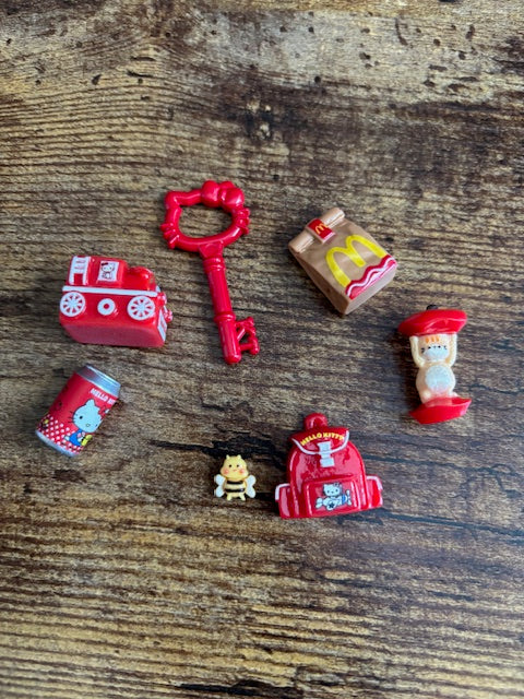 Collection of small toy items including a key, McDonald's inspired bag, and red train on a wooden surface
