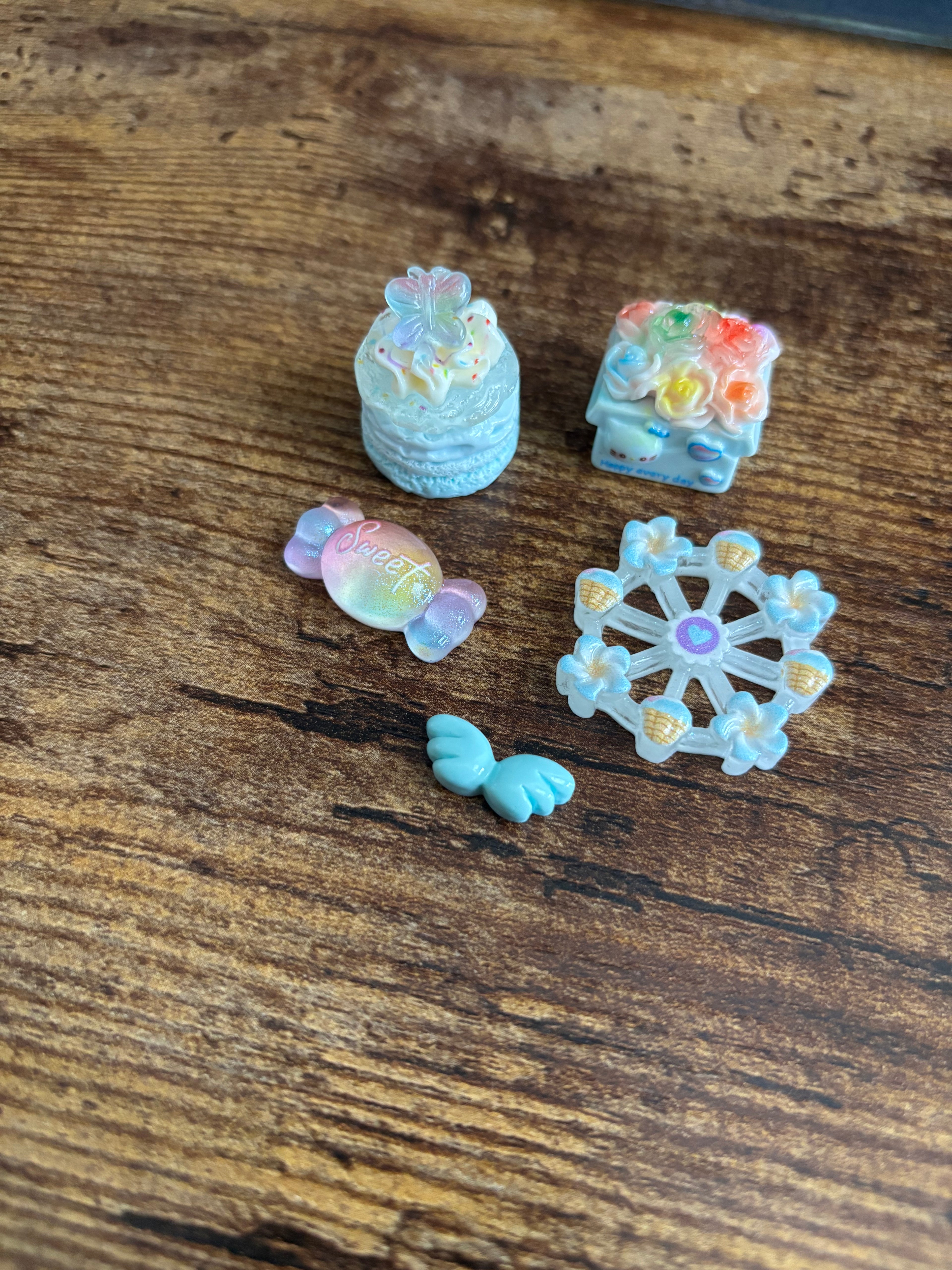 Five small decorative items - cake, flowers, candy, angel wings, and ferris wheel on a wooden surface