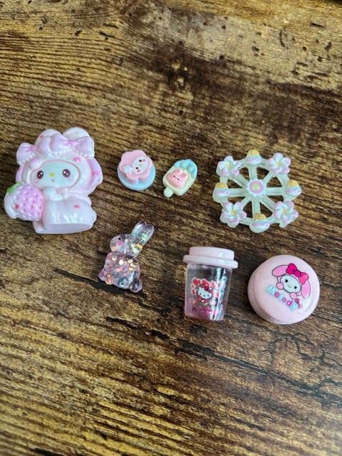 Set of small decorative items including a popsicle, ferris wheel, bunny, pink drink, cookie on a wooden surface.