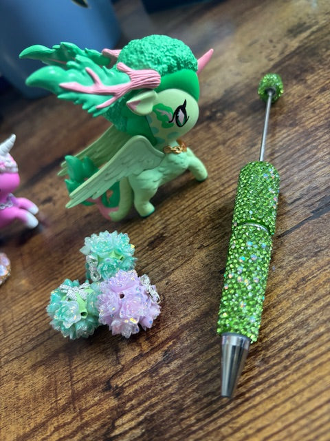 Green glittery pen with a dragon-Figurine topper on a wooden surface