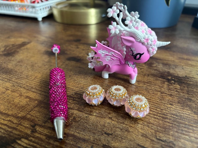 Pink pen, figurine, and fancy beads on a wooden surface