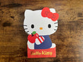 Hello Kitty paper notepad holding an apple and a box on a wooden surface
