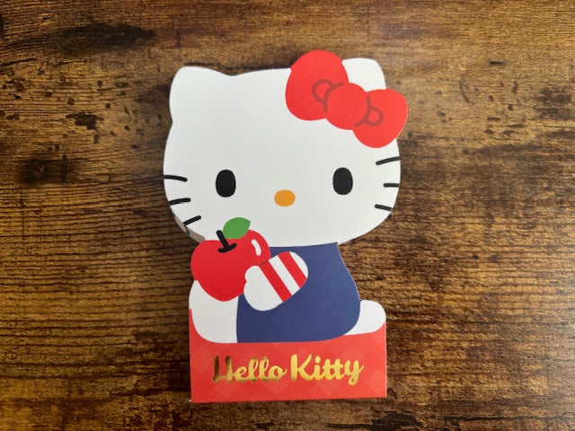 Hello Kitty paper notepad holding an apple and a box on a wooden surface