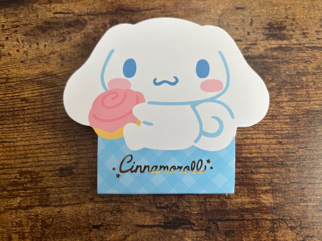 Cinnamoroll character Notepad holding a pink roll on a wooden surface