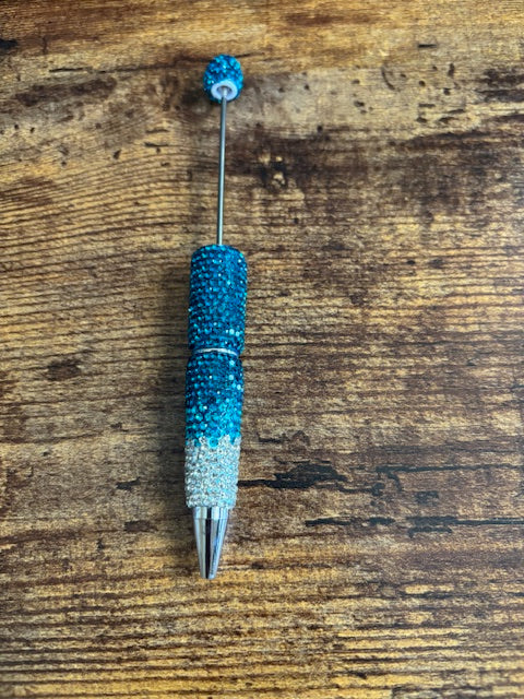 Decorative pen with blue glittery accents on a wooden surface